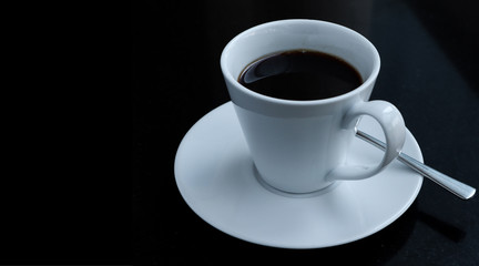black coffee in a coffee cup  top view with saucers and spoon on a black table.