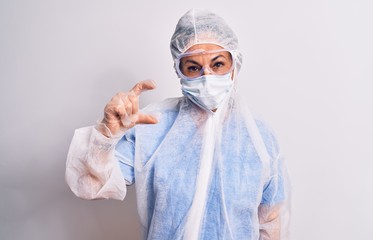 Middle age nurse woman wearing protection coronavirus equipment over white background smiling and confident gesturing with hand doing small size sign with fingers looking and the camera. Measure