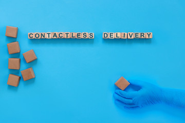Cardboard boxes with groceries or other purchases on a blue background. Hand in a medical glove with box. The inscription on wooden cubes "Contactless delivery."