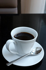 black coffee in a coffee cup  top view with saucers and spoon on a black table.