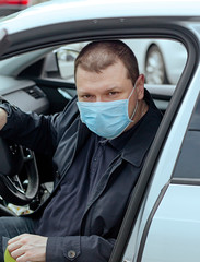 A young man in a protective mask drives a car. Portrait of a Caucasian man in a medical mask. A man is going to rest outside the city. Coronavirus covid-19, virus, pandemic. Virus protection concept