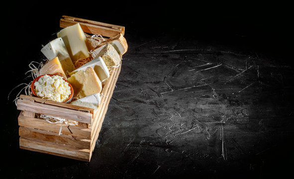 Different varieties of cheese in wooden box. Cheese delicacy on a black concrete background. Top view with copy space