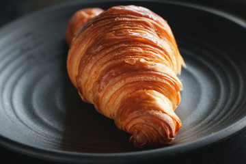 Classic crispy French butter croissant on a black plate. Dark photography     