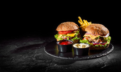 Two craft beef burgers with greens, red onion, cheese and vegetables on dark background. Delicious and attractive hamburger