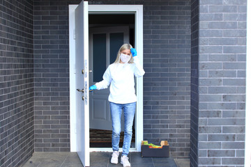 A young girl is standing on the porch of her house in a respiratory mask.