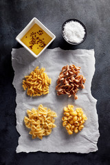 Variety of raw pasta with olive oil and salt on baking paper on black background