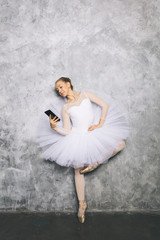 Fototapeta na wymiar Young ballerina classical ballet dancer using mobile phone against rustic wall