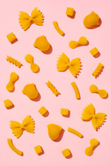 Variety of raw pasta arranged in a flat lay composition on pink background