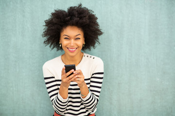 happy young african american woman holding mobile phone by green background