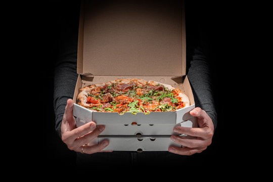 Man is holding and showing opened box with pizza on a dark background. Pizza delivery concept