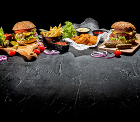 Delicious grilled burger with beef, tomatoes, cheese, cucumber and lettuce on a dark background. Top view with copy space. The concept of fast food and junk food
