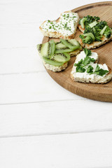 heart shaped canape with creamy cheese, broccoli, microgreen, parsley and kiwi on board on white wooden surface