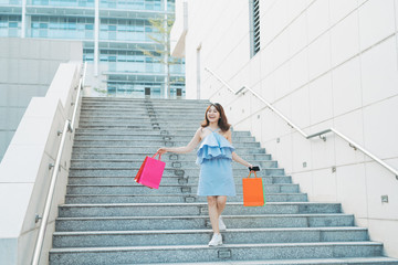 Beautiful young Asian going down stairs with colorful shopping bags. Shopping and fashion concept.