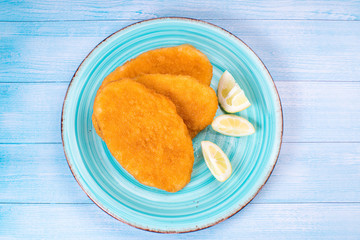 Top view, flat lay.Breaded chicken schnitzel on a blue plate with slices of lemon on a blue wooden...