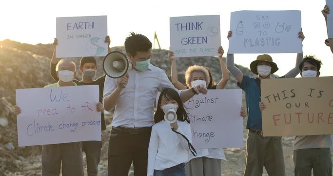 Group of mixed ages asian protestors making a protest about global warming and plastic pollution with climatestrike ecology poster on a huge garbage dump from landfill. Slow motion.