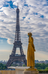 Paris, France - 05 06 2020: Golden statue of a woman wearing a surgical mask during confinement against coronavirus and the eiffel tower