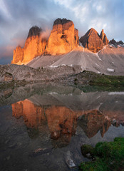 Mountain lake reflecting the mountains of the Three Peaks in the European Dolomite Alps with alpenglow during sunset, heavy clouds in the sky, South Tyrol Italy.