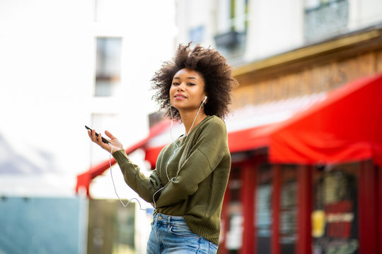 Side Of Young Black Woman Listening To Music With Earphones And Smart Phone In City