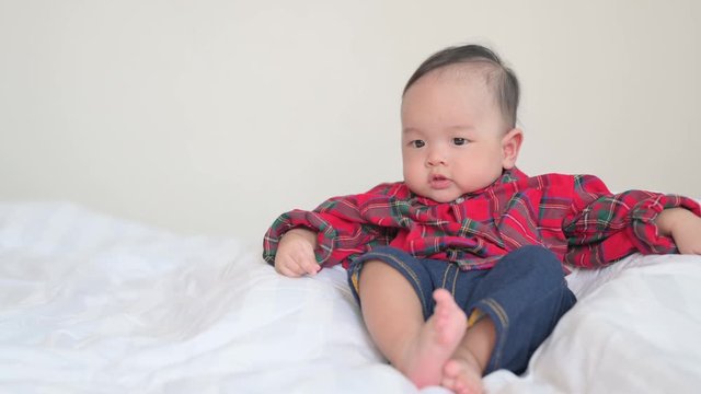 Asian baby playing at home in bedroom.Funny baby boy trying to sit on bed.