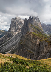 Obraz premium Dramatic mountain peaks of Seceda with heavy clouds in the European Dolomite Alps, meadow in the foreground, steep cliff, South Tyrol Italy.