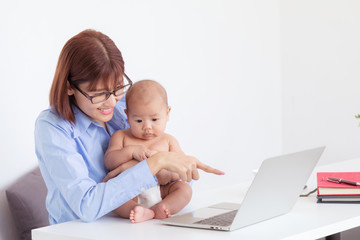 Beautiful Asian mother multitask nurture newborn at home office, employee work from home feeding, playing, holding, smiling with toddler, mother take care baby and working with laptop technology
