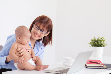 Asian mother stop working pay attention to crying baby, baby get sick naughty mother on desk with laptop multitask motherhood take care toddler at home office, small business entrepreneur feeding baby