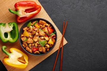 Gai Pad Med Mamuang or Thai Cashew Chicken in black bowl on dark slate backdrop. Kai Med Ma Muang is thai cuisine dish with chicken meat, capsicum, onion, scallions, chilli. Thai Food. Copy space