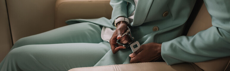 cropped view of african american businesswoman fastening safety belt in private jet