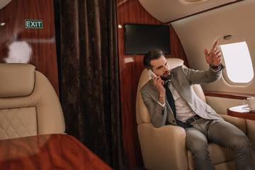 Obraz premium handsome businessman talking on smartphone and pointing with finger in private jet