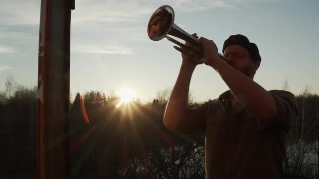 a man in a che Guevara beret with a trumpet plays against the background of the sunset. the sun's rays hit the lens. celebration of life.