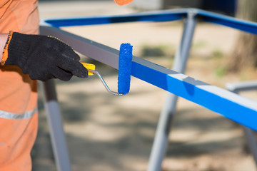 Worker in gloves with a roller paints metal blue