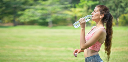 young fitness woman drinking water from plastic bottle after exercise at public park in morning ....