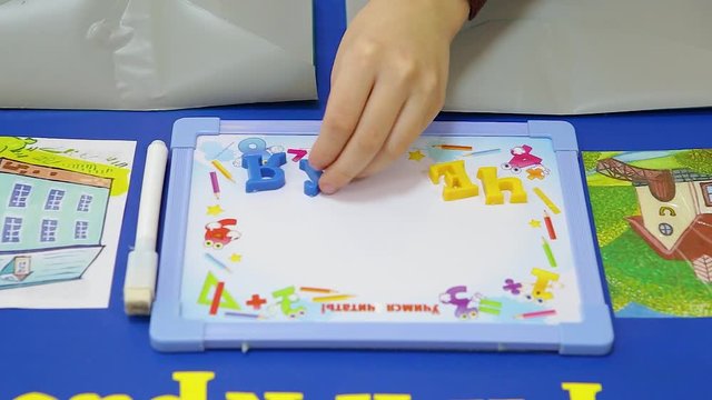 The kids put the letters on the table. The letters are colored. There is a white board on the table. Close-up