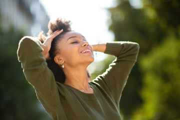 Close up carefree young black woman smiling outdoors with hand in hair