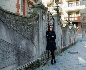 Nice, brunette woman wearing in black coat walking in old city. Smile, cute girl in Batumi, Georgia. Spring time.
