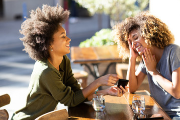  two female friends sitting at outdoor cafe with mobile phone