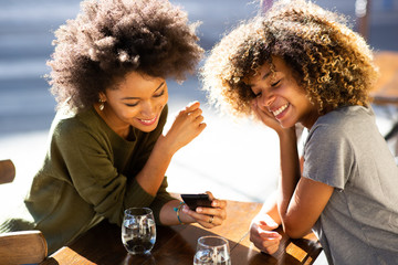 two young african american women sitting at outdoor cafe looking at cellphone