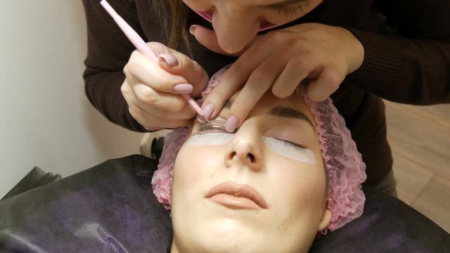Beautician applies a special wellness mixture on client eyelashes close up view. Professional procedure laminating and Botox eyelashes modern healing. Silicone curlers or rollers for curling