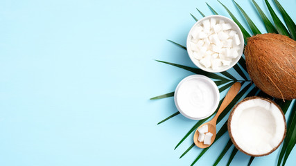 Coconut oil cosmetic cream and palm leaf on blue background top view. Skin care, body and hair treatment concept.