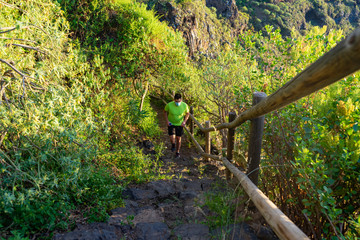 Man with mask running down a path. The corridor is in a forest. The photo was taken in Tenerife, an ideal place to practice trail running. In his hand he has a bottle of water (Soft flask).