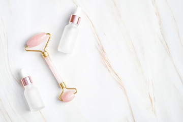 Face massage roller and two dropper bottle with essential oil on marble background. Flat lay, top...