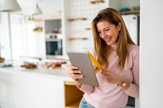 Woman In Kitchen Looking At Recipe On Tablet