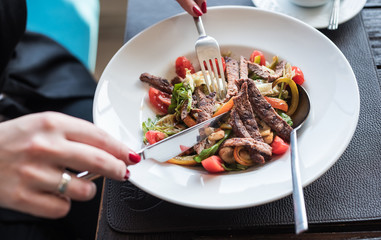 Meat salad at restaurant. The girl eats salad with tableware.
