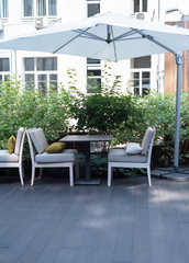 Wooden table and two stylish chairs under a white umbrella.