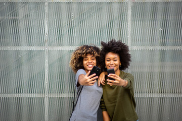 two happy young black women taking selfie with cellphones