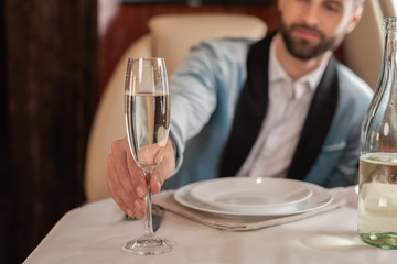 selective focus of elegant man taking glass of champagne from served table in private plane