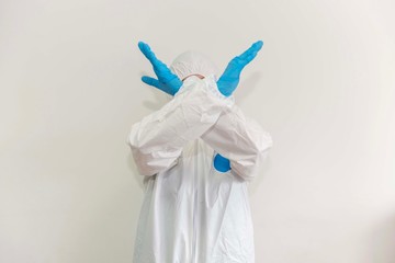 Front view of a doctor covering her face with crosswise hands. She wears gloves and a protective suit. Covid 19 emotional reaction. coronavirus pandemic. Without face. Copy Space
