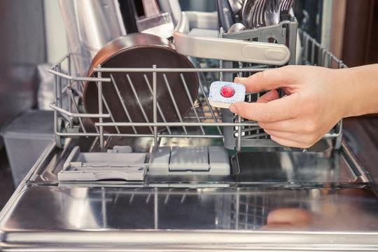 hand holds detergent on the background of the dishwasher