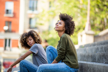 Side of two cool young african american women sitting on steps outside