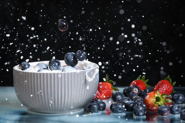 Milk splash close up of falling berries in a grey plate of milk. Mix of blueberries and strawberries . Healthy diet. Organic food. Black background.	